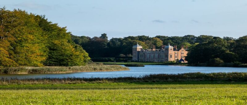 Blickling Hall, A stately home with a lake and trees in the foreground.